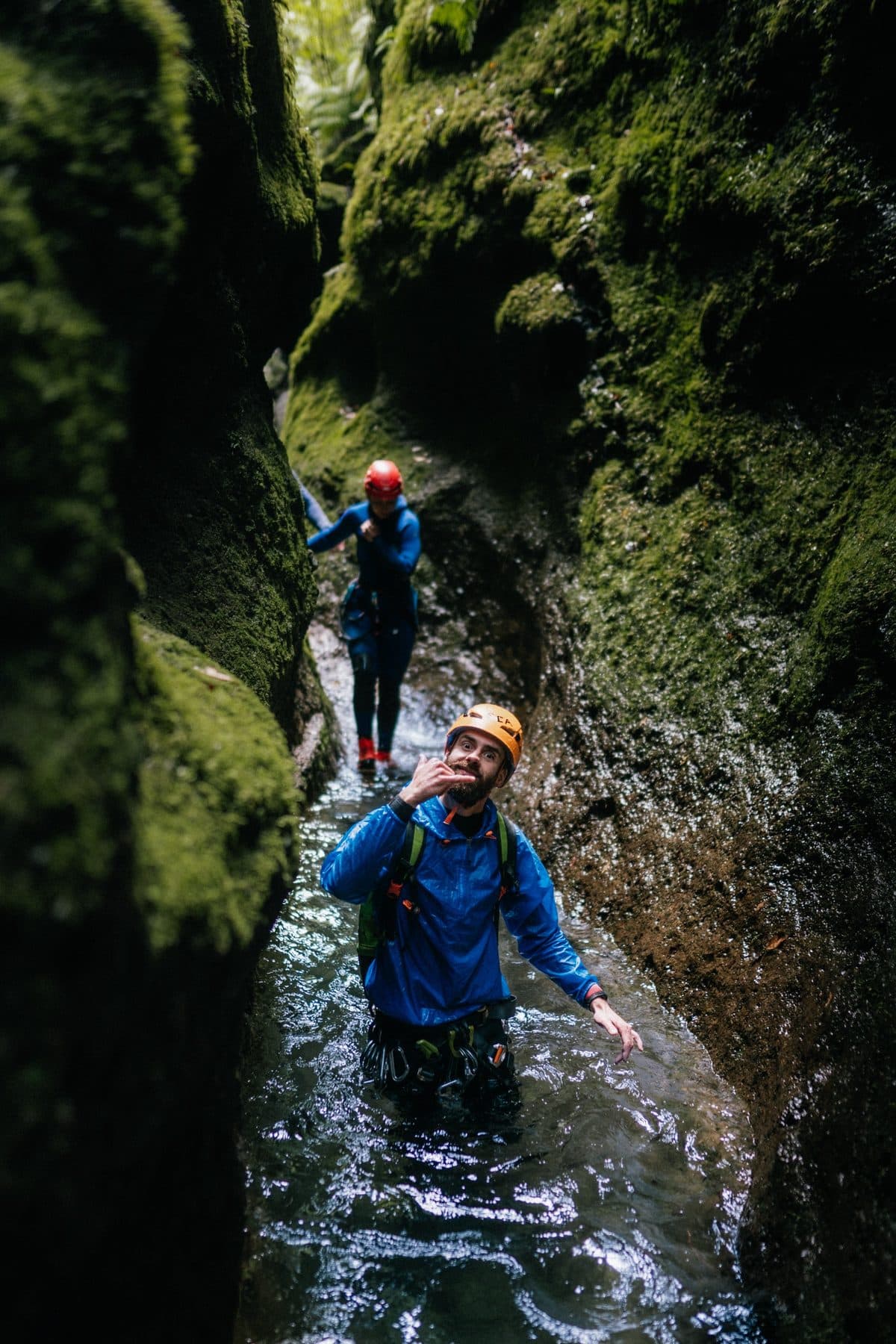Caminando por el agua en un barranco estrecho cubierto de musgo, con chaqueta impermeable