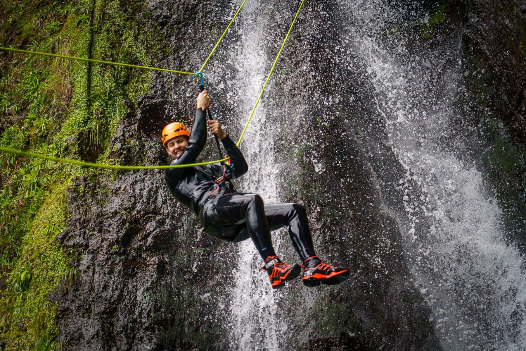 Un cliente cruzando una cascada colgado de una cuerda en Madeira